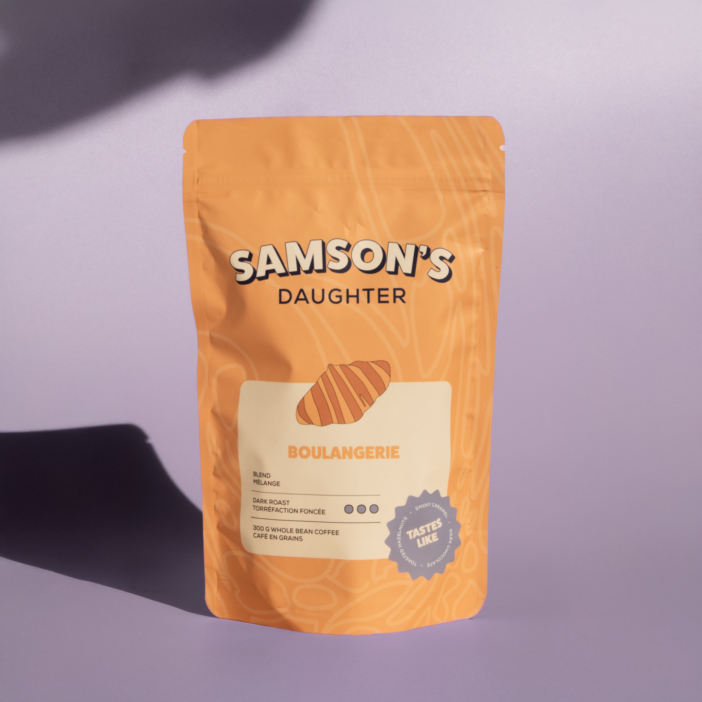 A bag of Boulangerie dark roast with a purple background in hard light.