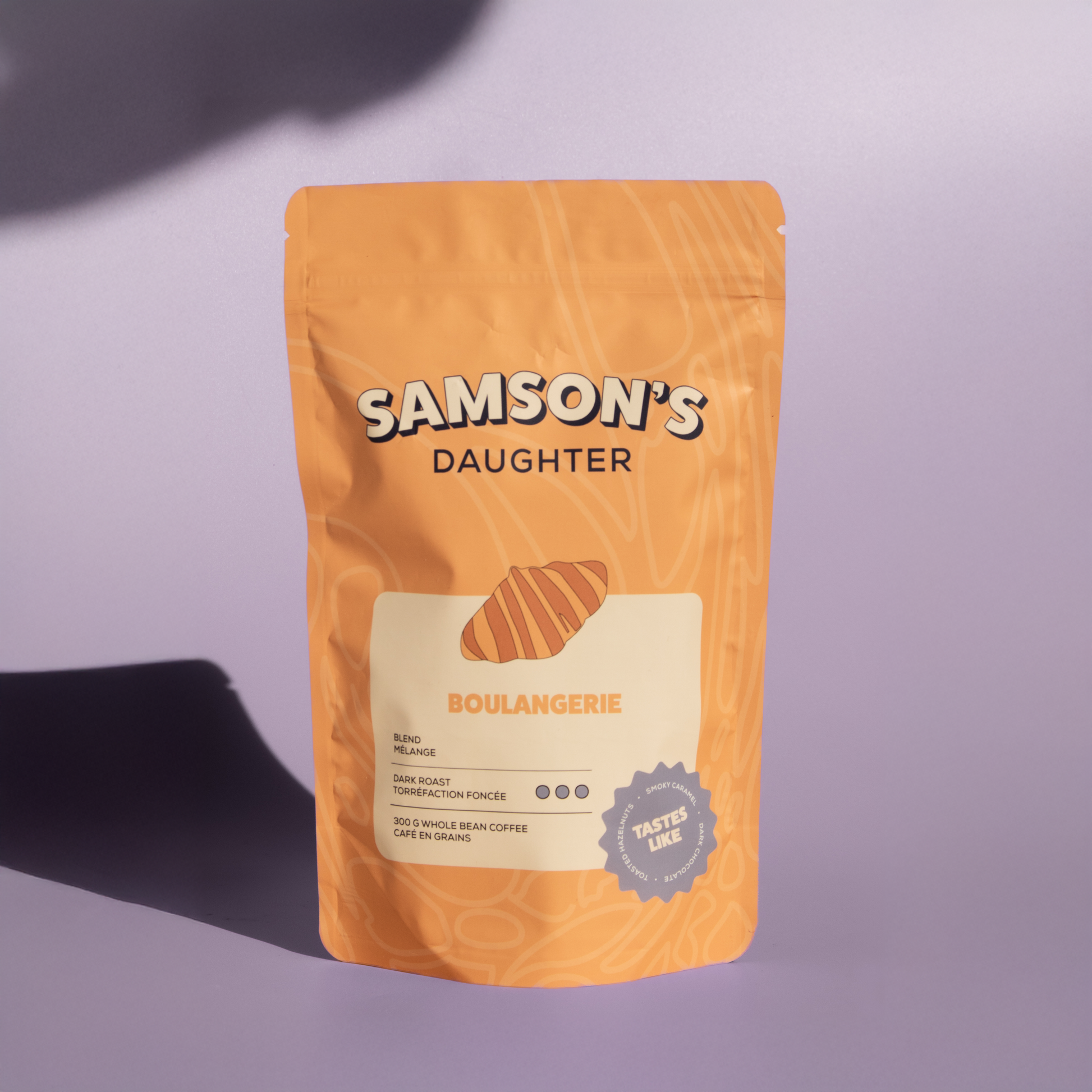 A bag of Boulangerie dark roast with a purple background in hard light.