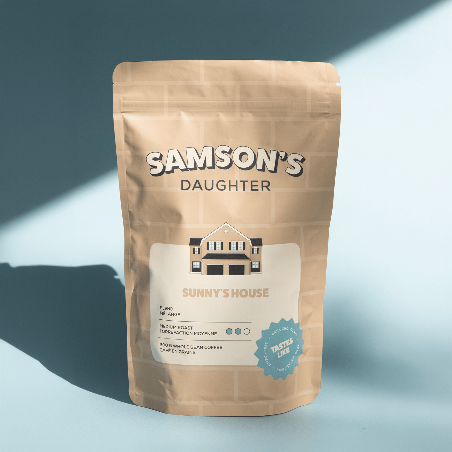 A bag of Sunny's House medium house blend with a light blue background in hard light.