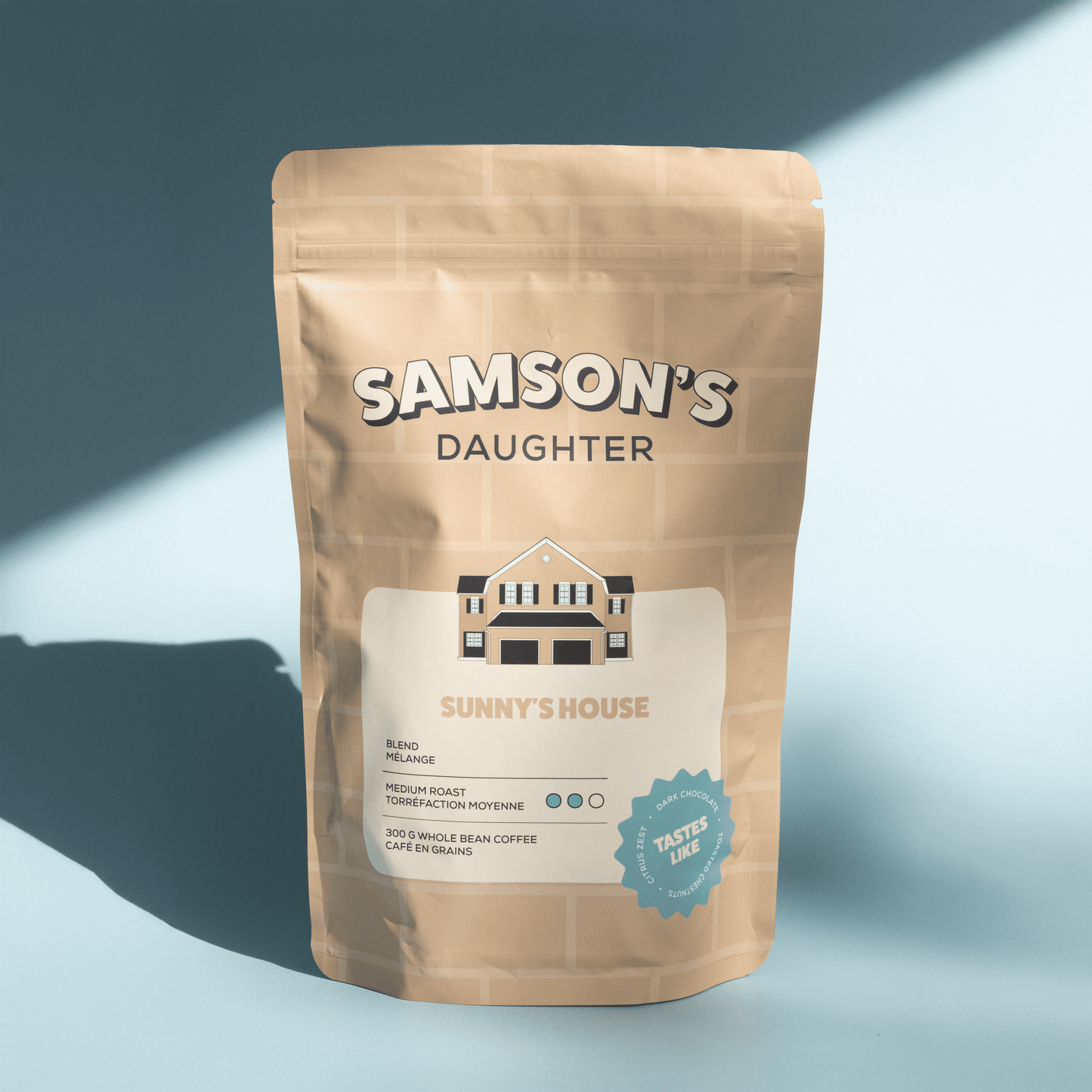 A bag of Sunny's House medium house blend with a light blue background in hard light.